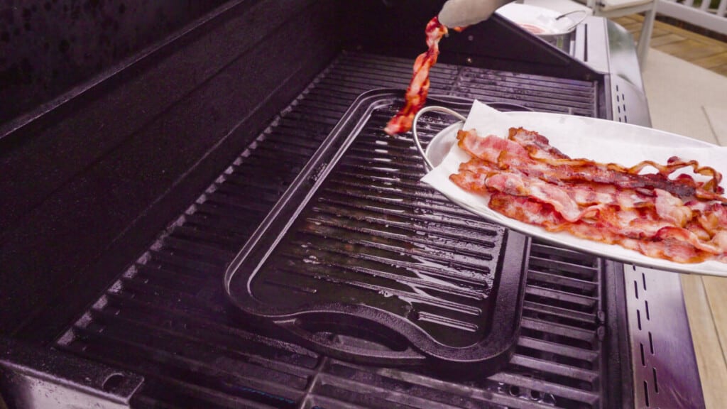 A cast iron griddle on a gas grill just about to cook ba.