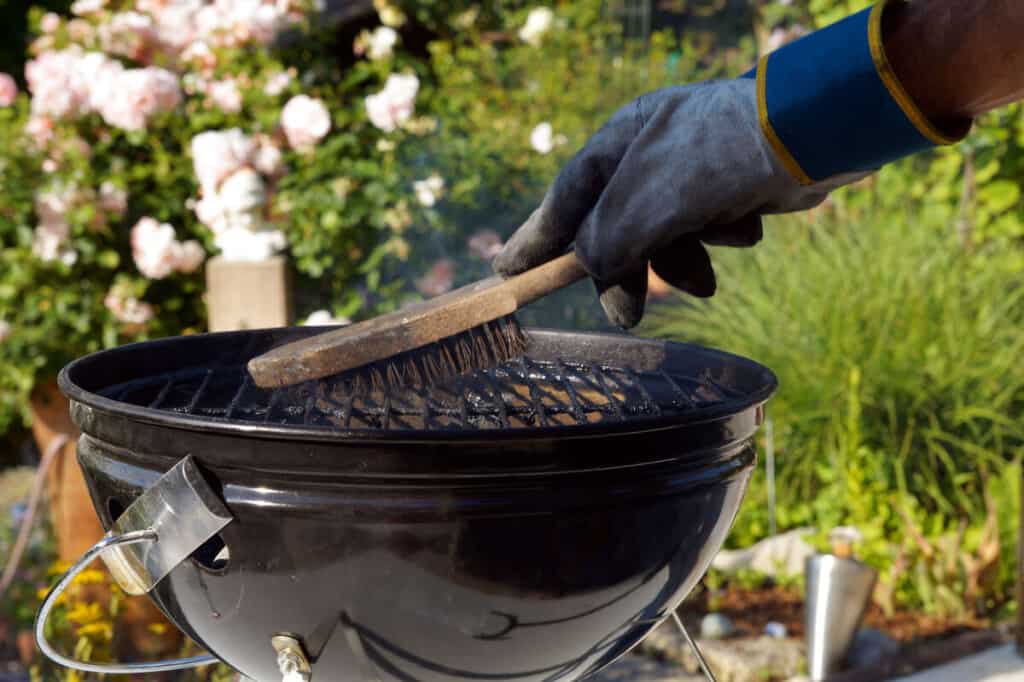 Someone brushing off hot grill grates while wearing gloves for grill.