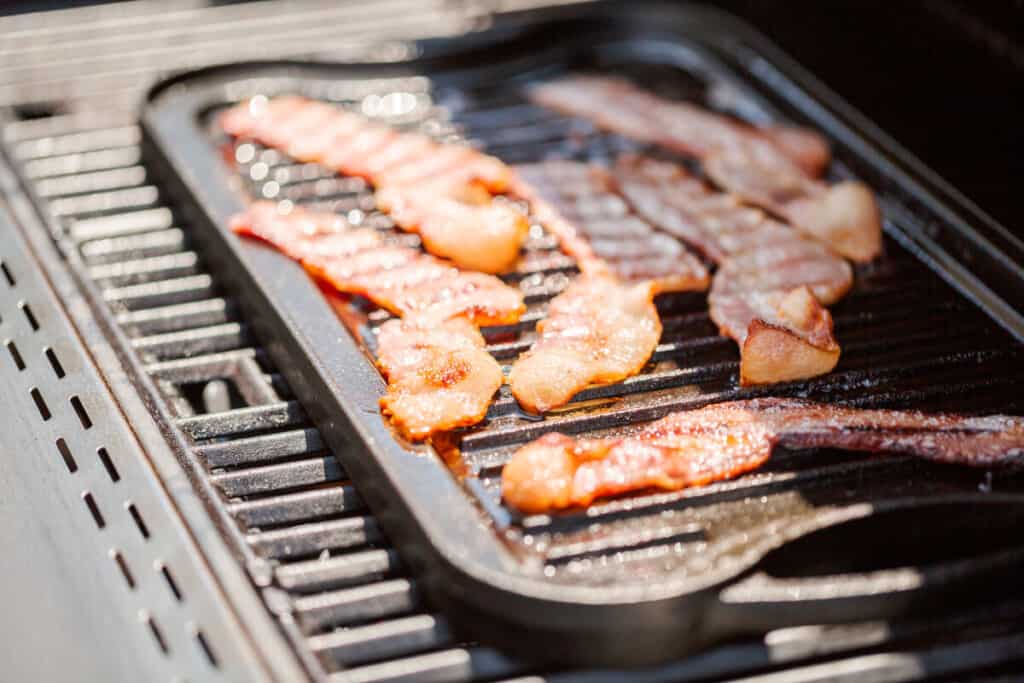 A griddle placed on a grill cooking bacon