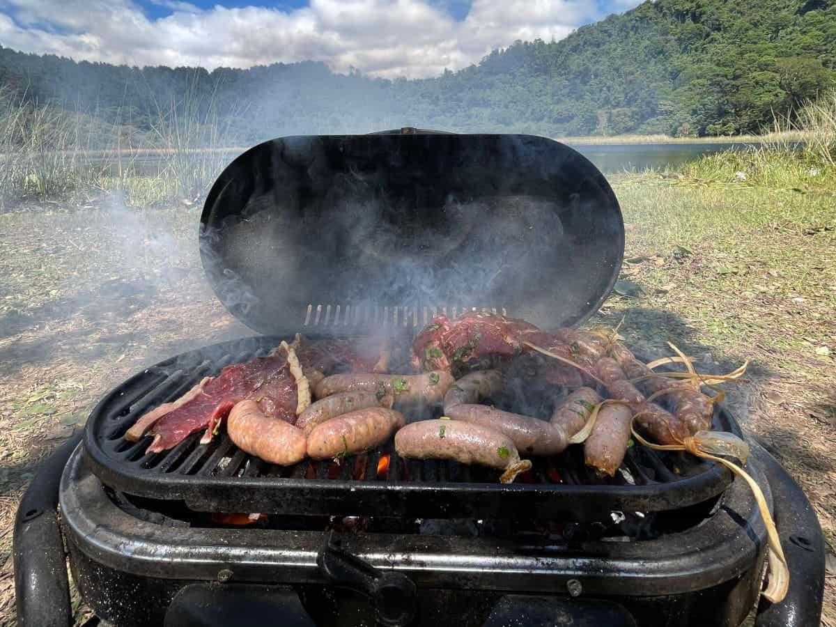A travel gas grill with lid open, with a mountain view in the backgro.