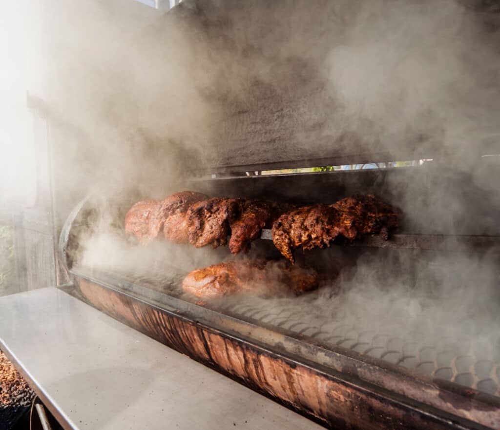 A large quantity of meat inside large charcoal smoker