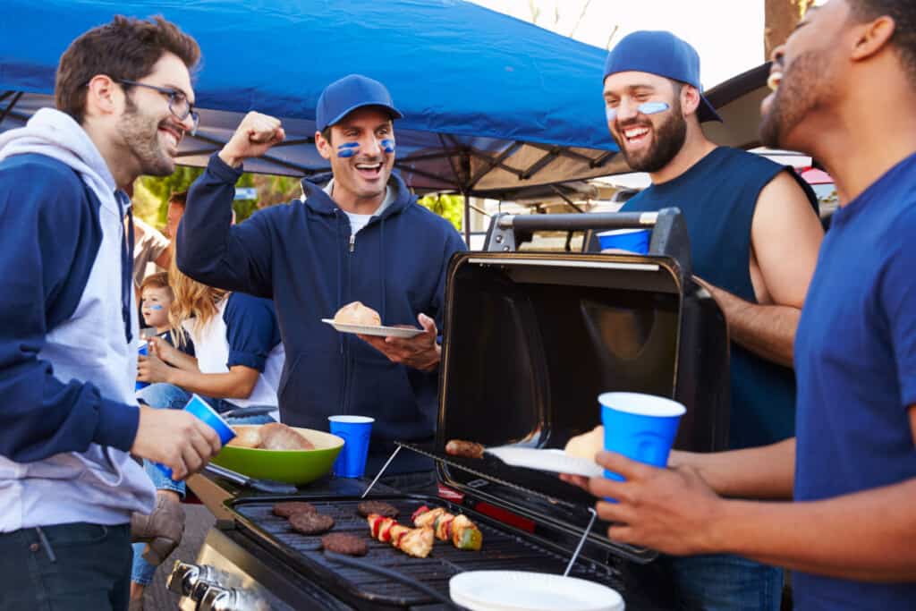 A group of people dressed in blue crowding around a tailgate gri.