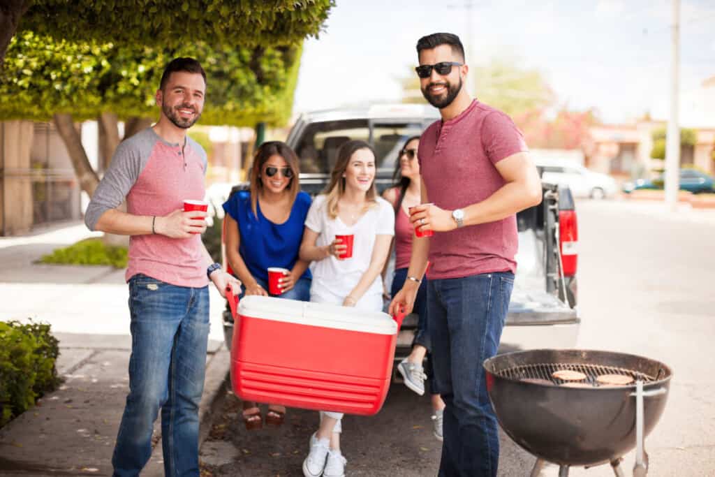 Small group of people sitting on a tailgate in front of a gr.