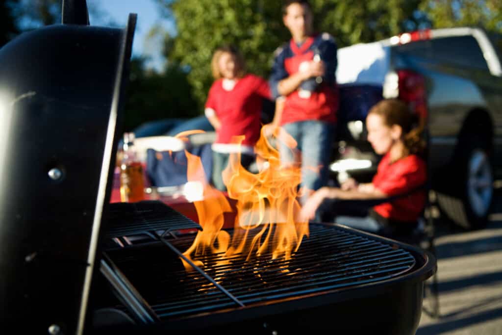 Tailgate grill in foreground, blurred party of people in the backgro.