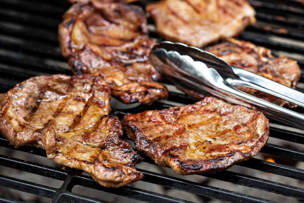 A pair of tongs flipping pork chops on a gr.