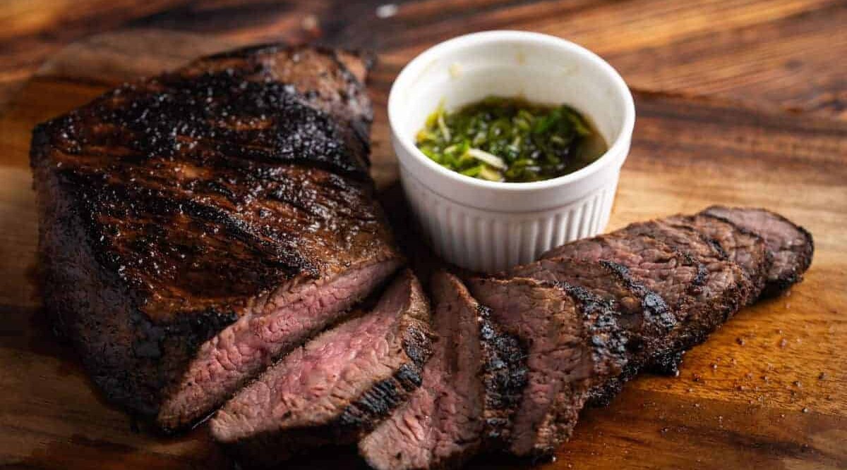 A grilled tri-tip roast, sliced and sitting on a wooden surface.