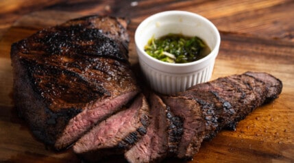 A grilled tri-tip roast, sliced and sitting on a wooden surface.