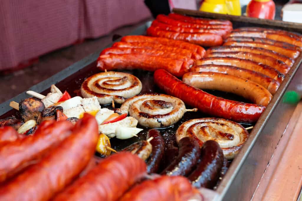 A flat top grill cooking many different types of sausa.
