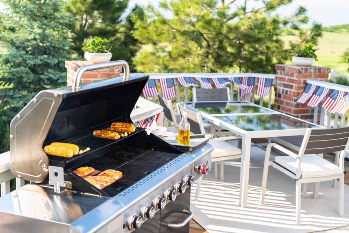 A gas grill on a patio with garden furniture in the background.