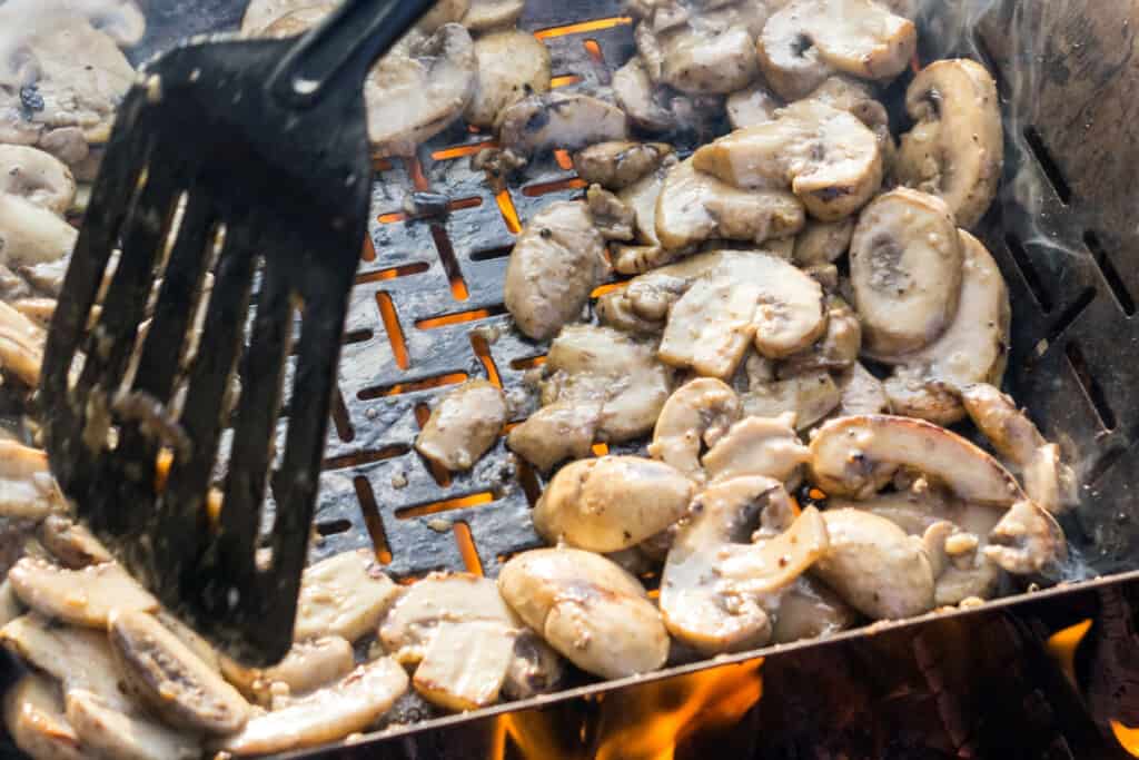 A plastic spatula turning mushrooms on a hot gr.