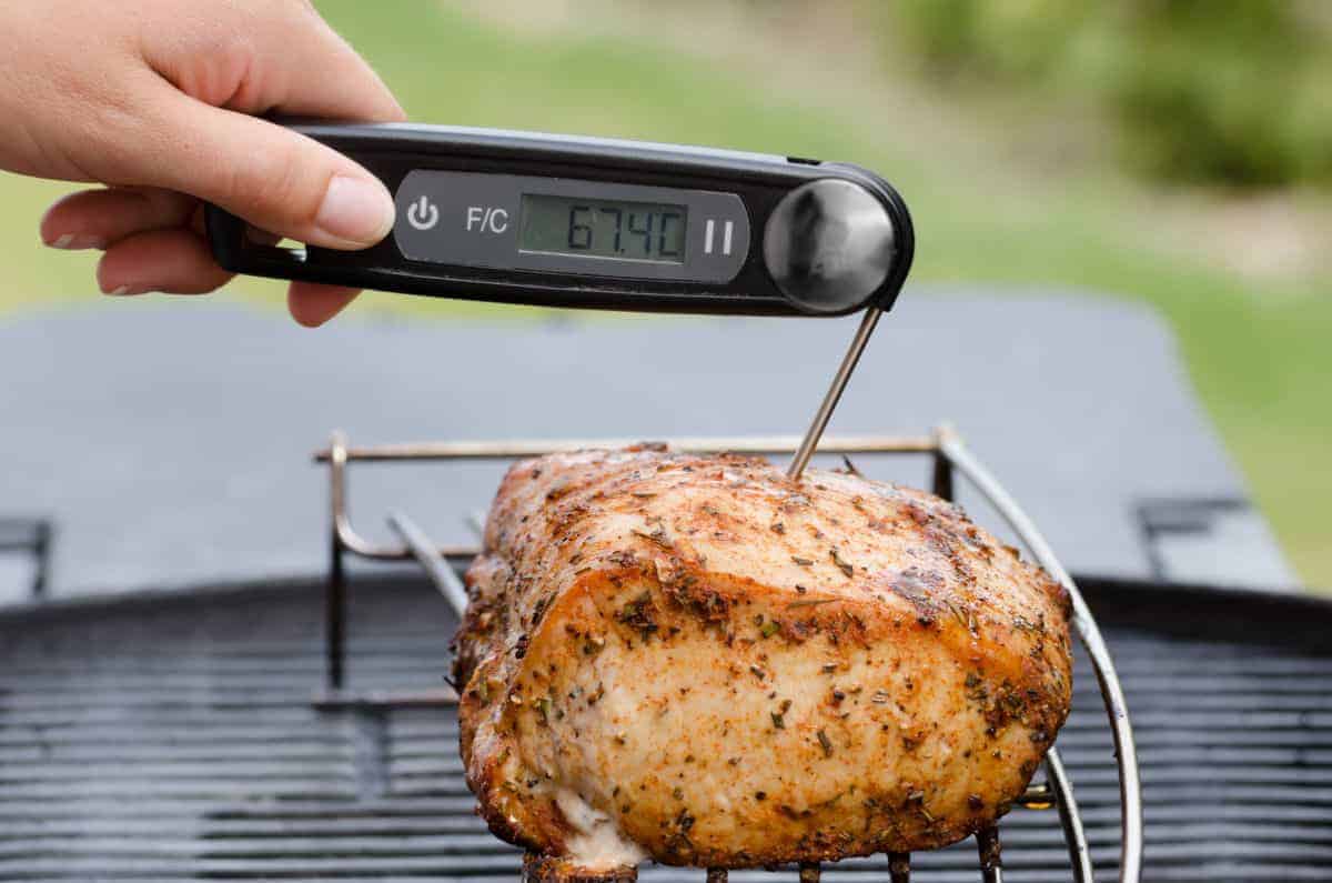 The temperature of some meat on a BBQ being taken by an instant read thermometer