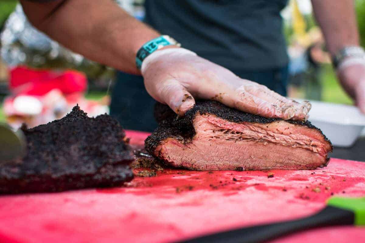 A man slicing barbecue smoked brisket on a red cutting board.
