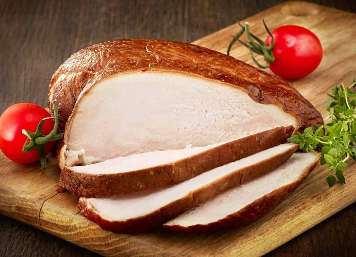 Smoked and sliced chicken breast on a cutting board with cherry tomat.