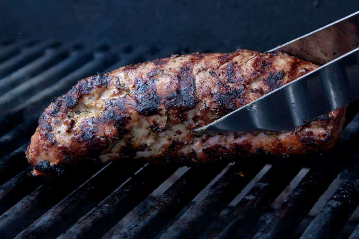 pork tenderloin held in tongs in a smo.