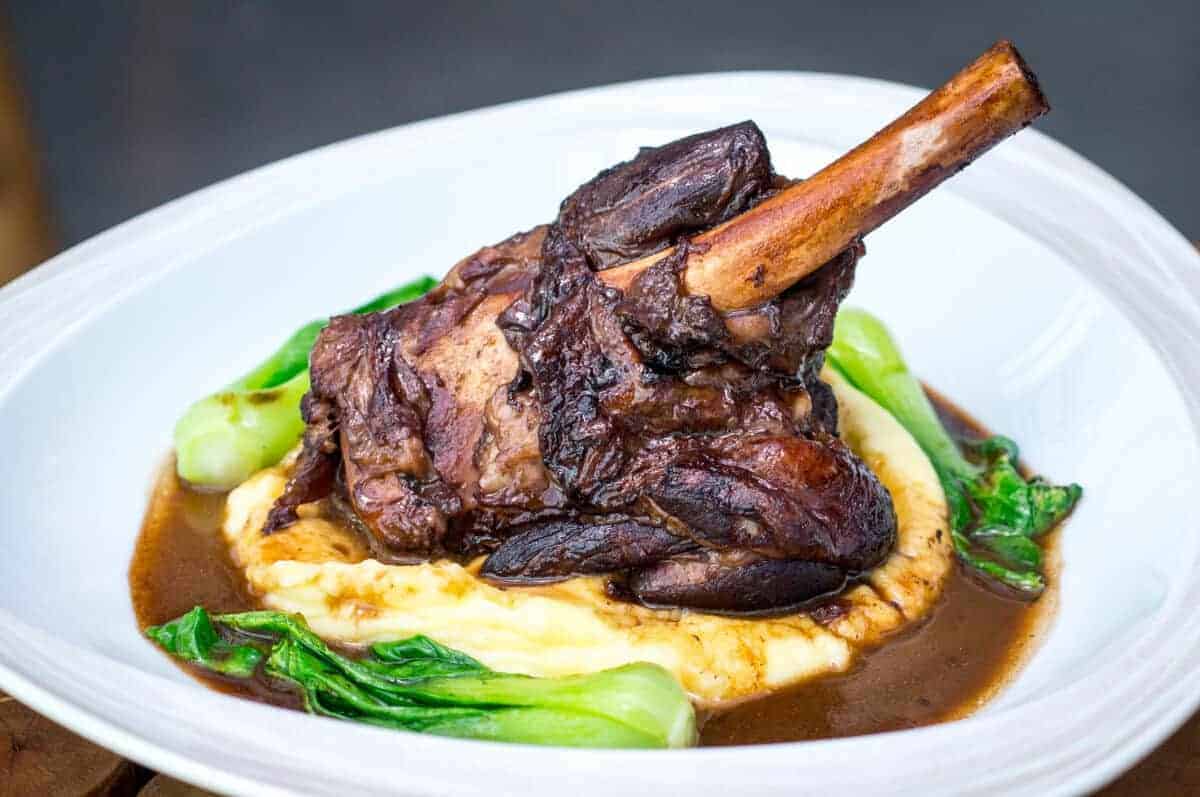 A smoke roasted lamb shank, on a bed of mash with gre.