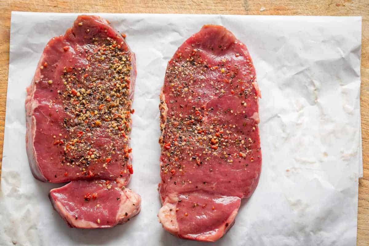 Two ranch steaks on butcher paper with a peppery season.