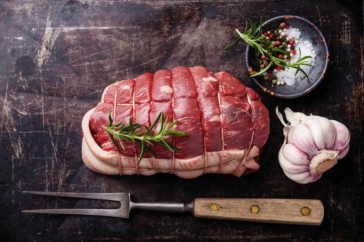 A raw, tied rump roast on a cutting board with rosemary