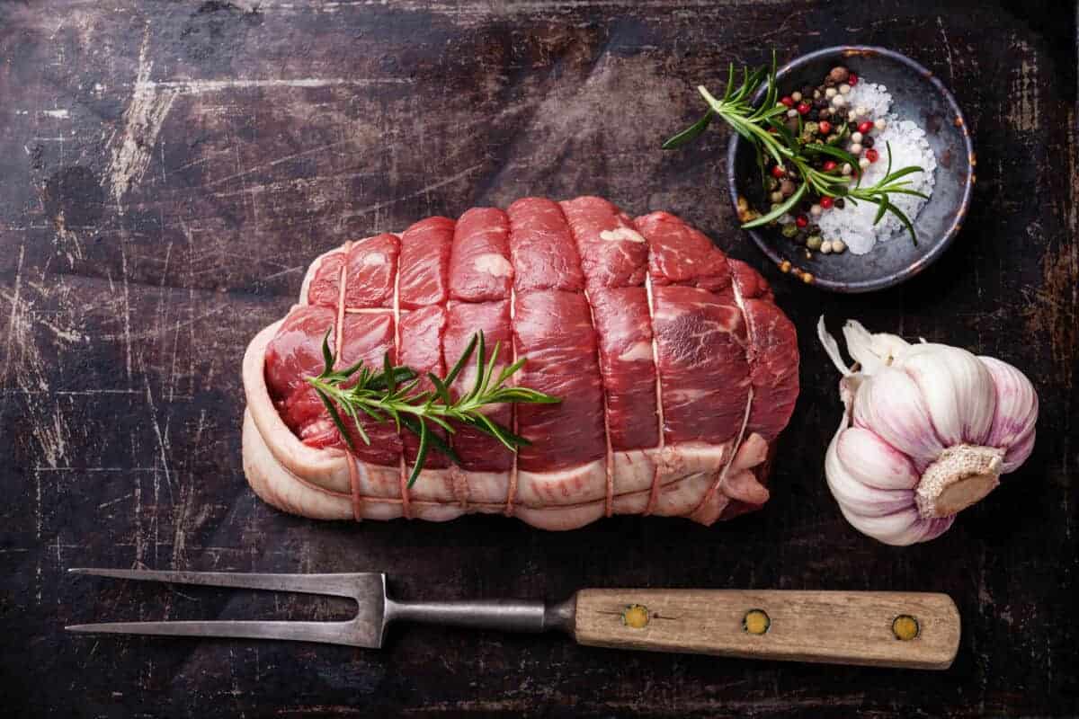 A raw, tied rump roast on a cutting board with rosem.