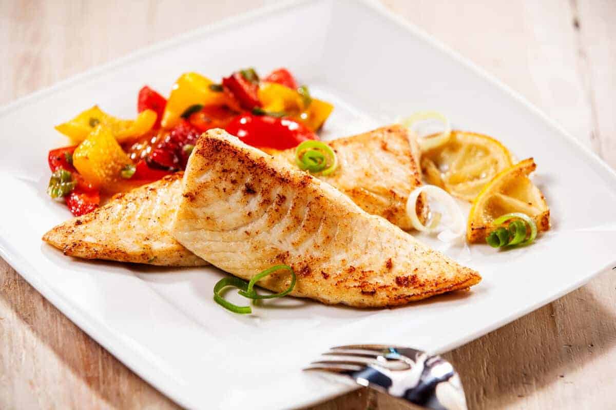 Smoked tilapia filet in a bowl with red and yellow pepp.