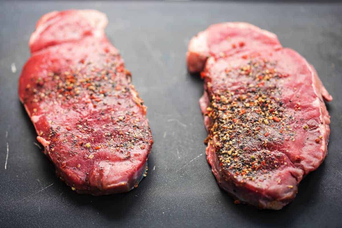 Two well seasoned ranch steaks on a dark surface
