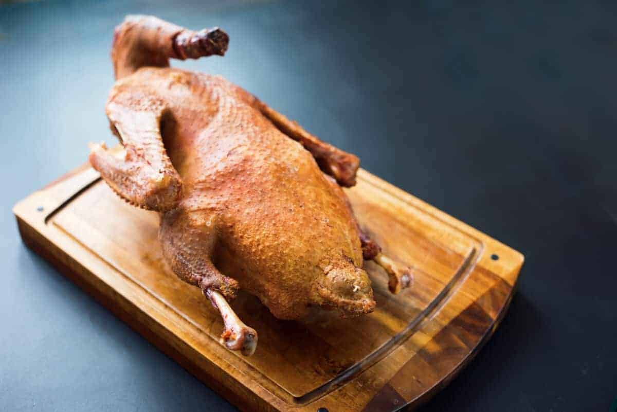 A whole smoked duck on a wooden board
