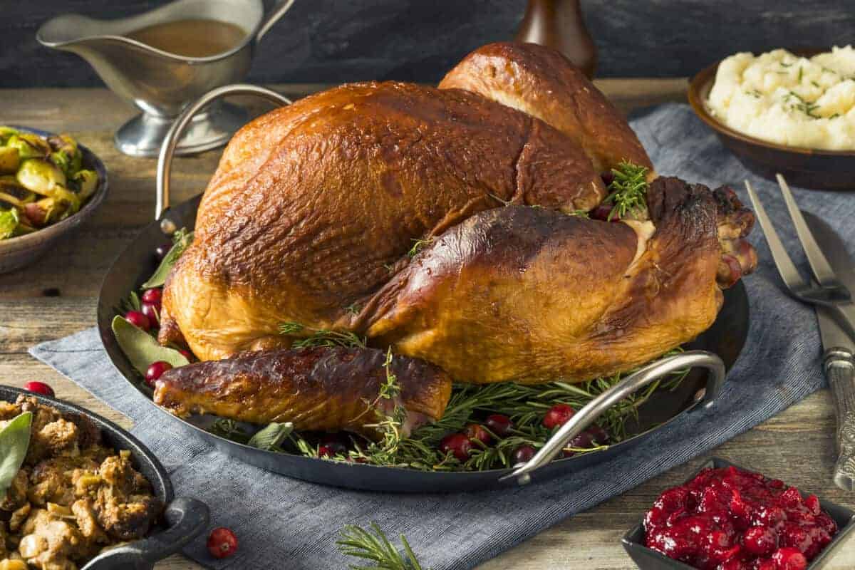 A whole smoked turkey on a tray with herbs and cranberries