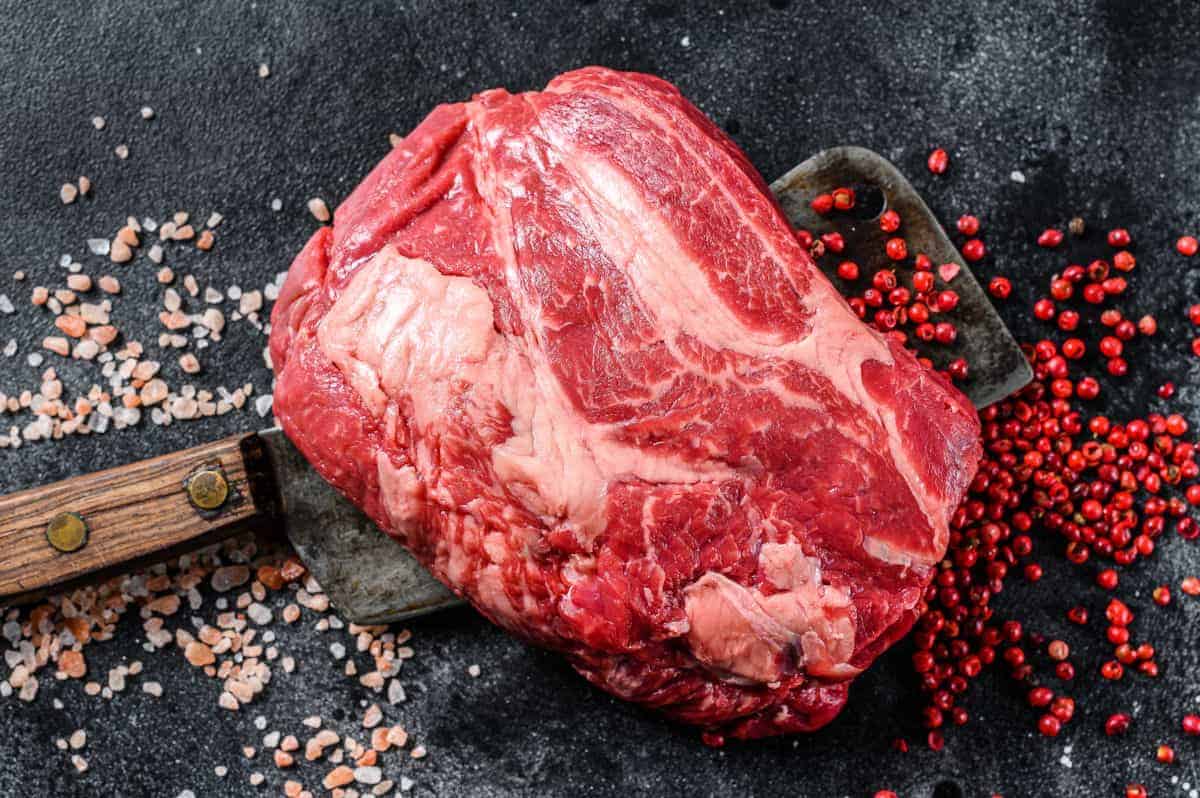 A raw chuck eye roll on a large butchers cleaver, with pink peppercorns and pink sea salt