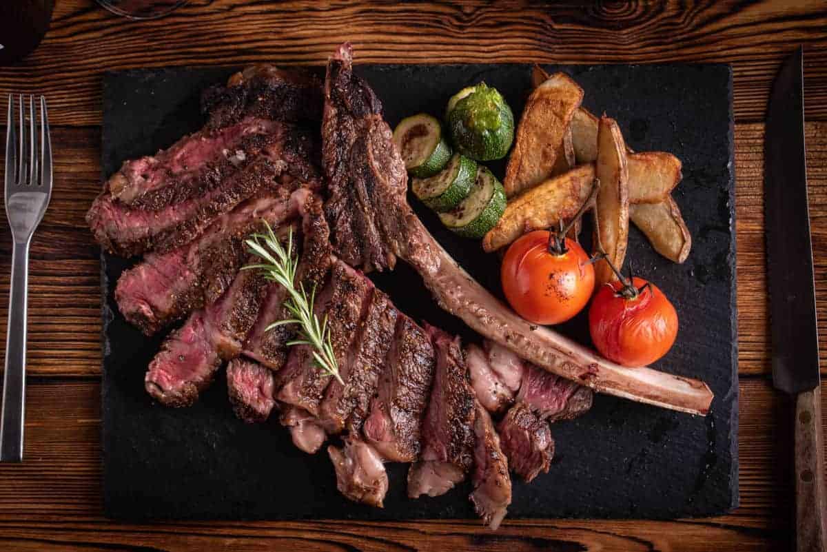 A grilled and sliced tomahawk steak on a cutting board with tomat.