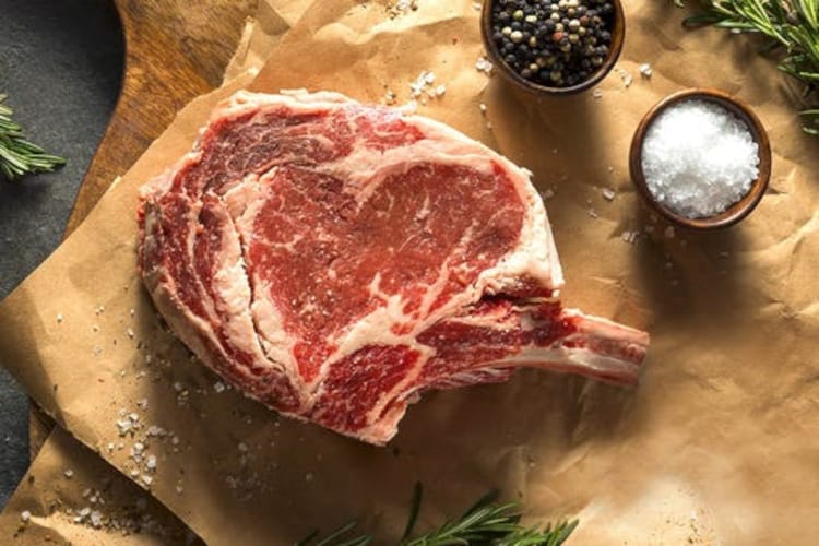 crowd cows tomahawk steak on brown butcher paper, with pots of salt and pep.