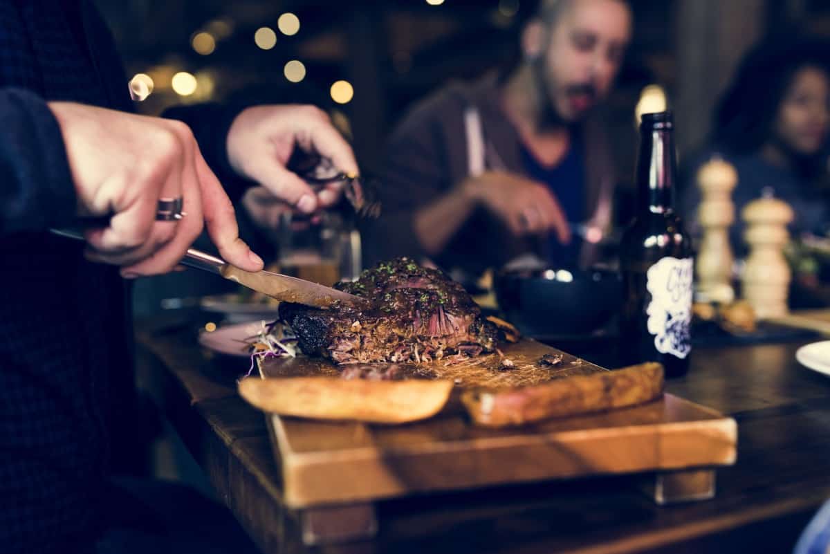 A restaurant scene with a close up of mans hands slicing and eating a steak