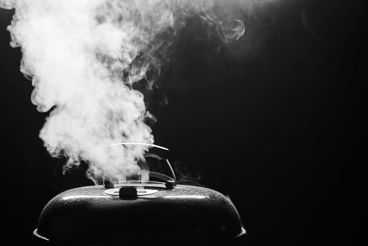 A dark image of a grill with smoke coming out of the top v.