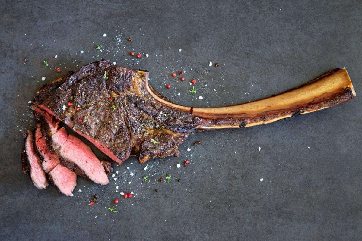 Grilled then sliced tomahawk steak on a dark surface
