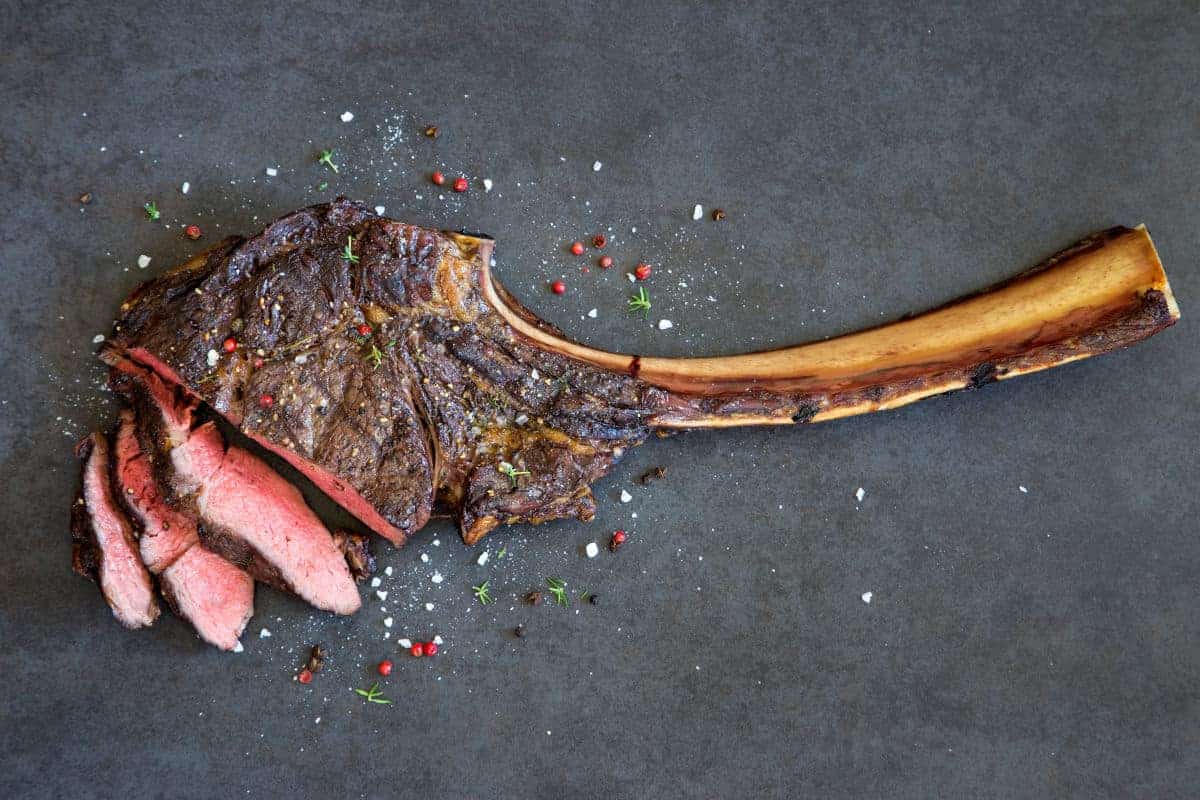 Grilled then sliced tomahawk steak on a dark surf.