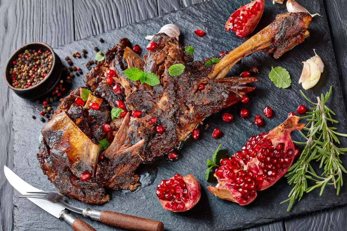 A smoked lamb shoulder on a dark surface with pomegranate se.