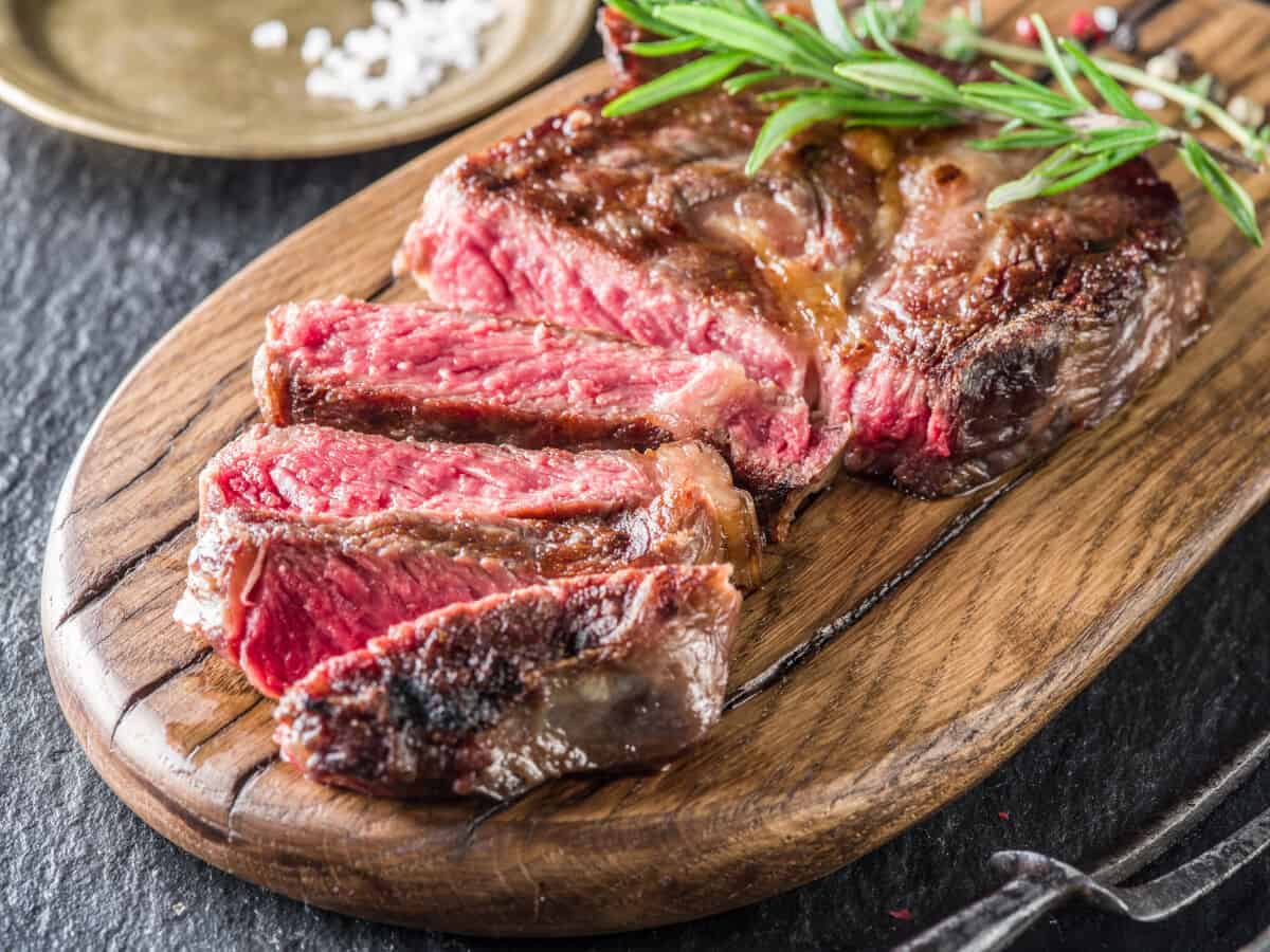 A medium rare ribeye steak, sliced on a cutting board with salt and rosem.