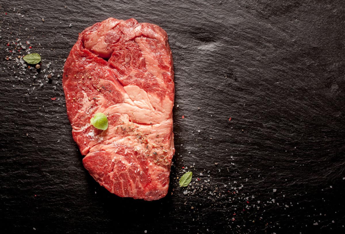 raw chuck eye steak on a dark surface with salt flakes