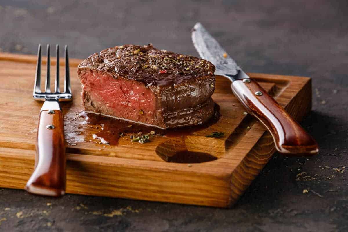 A grilled and sliced filet mignon on a cutting board with a kn.