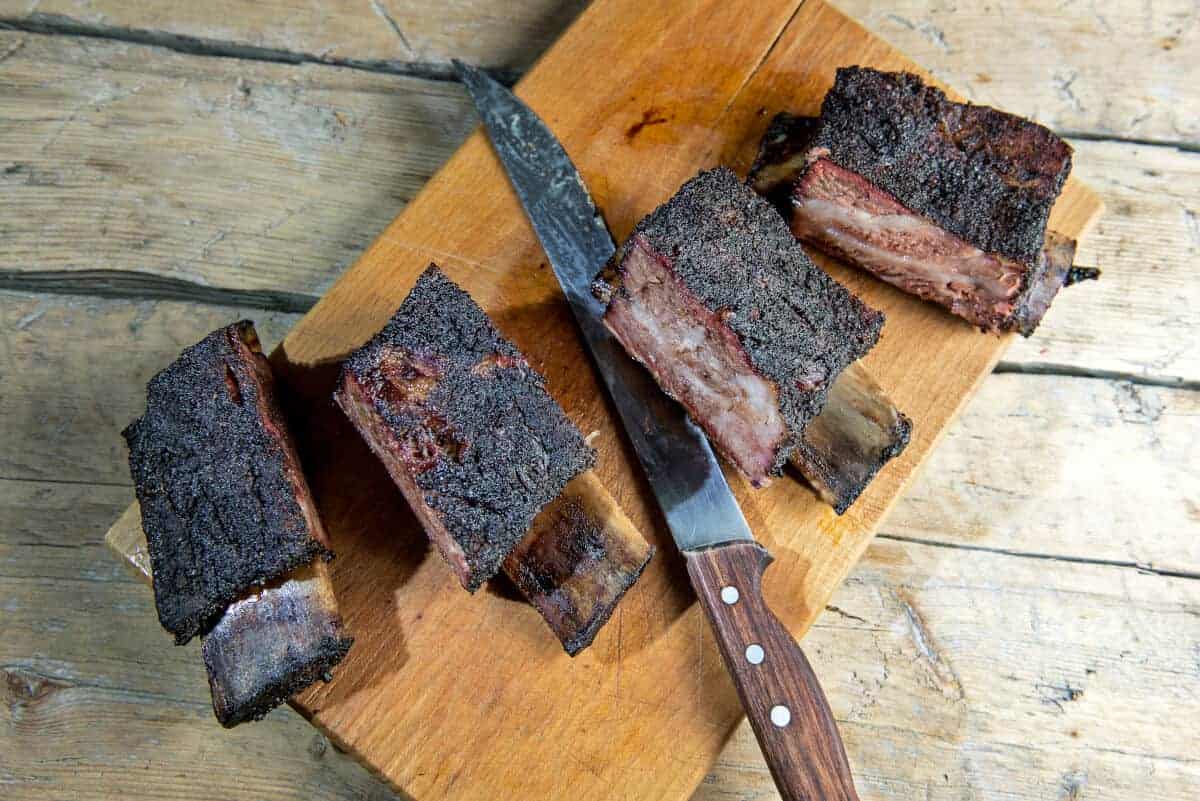 Four smoked beef short ribs, sliced on cutting board with kn.