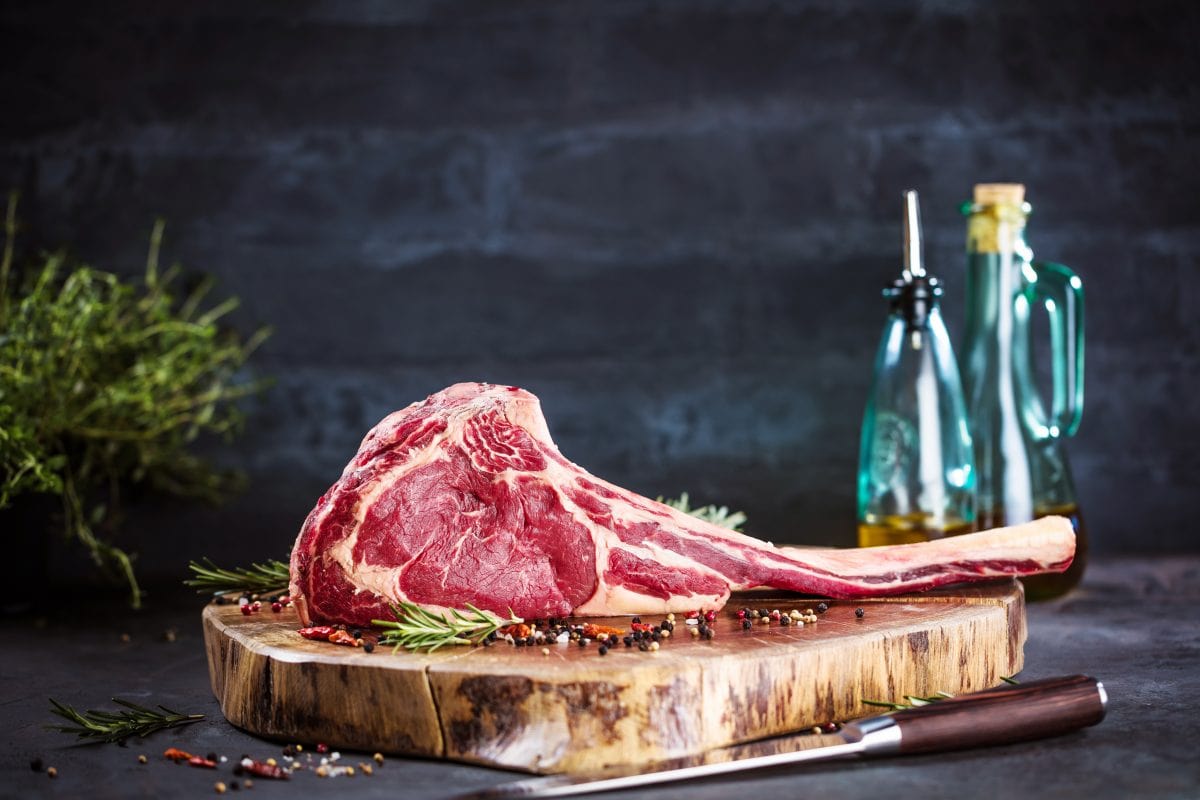 A raw tomahawk steak stood up on a rustic cutting bo.