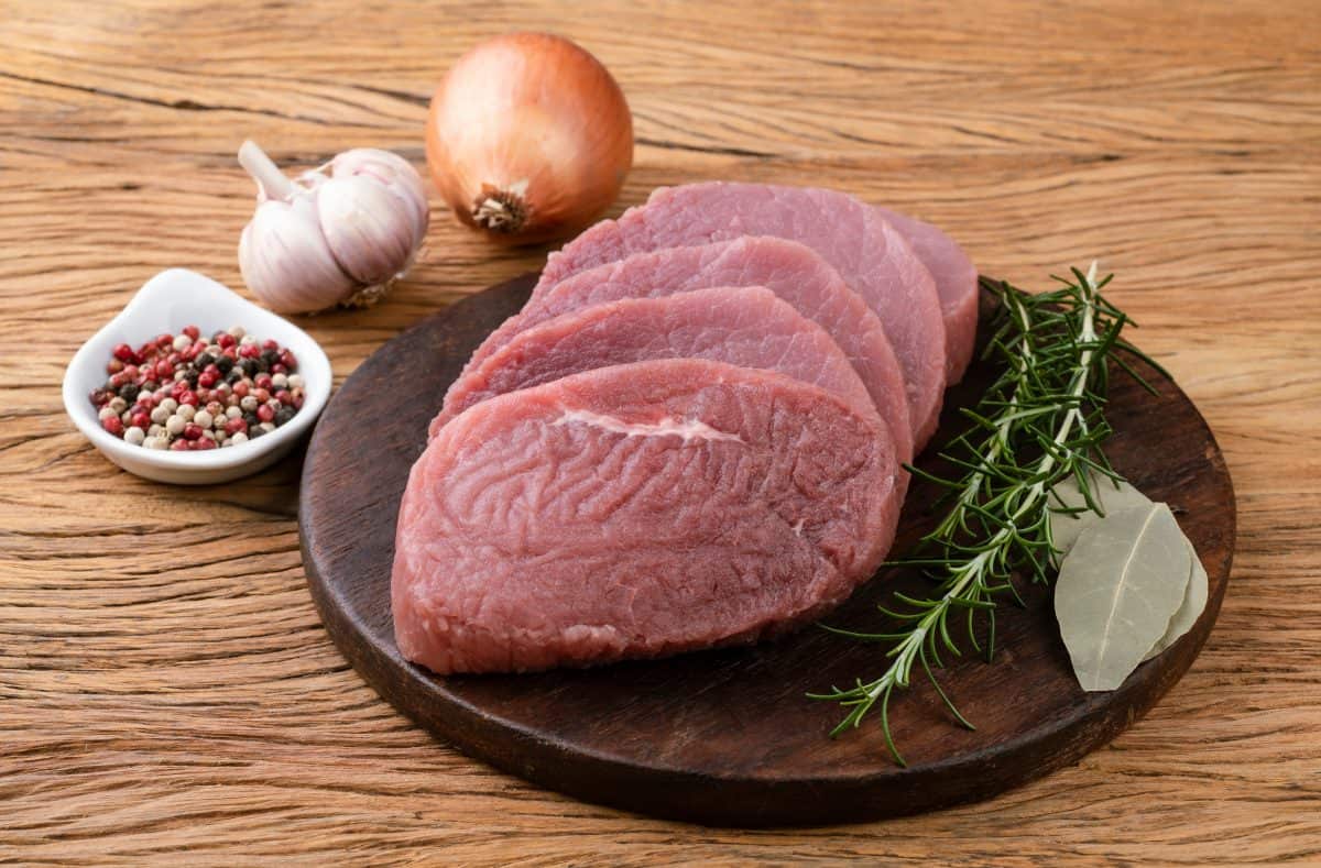 4 eye of round steaks on a wooden cutting board with rosem.