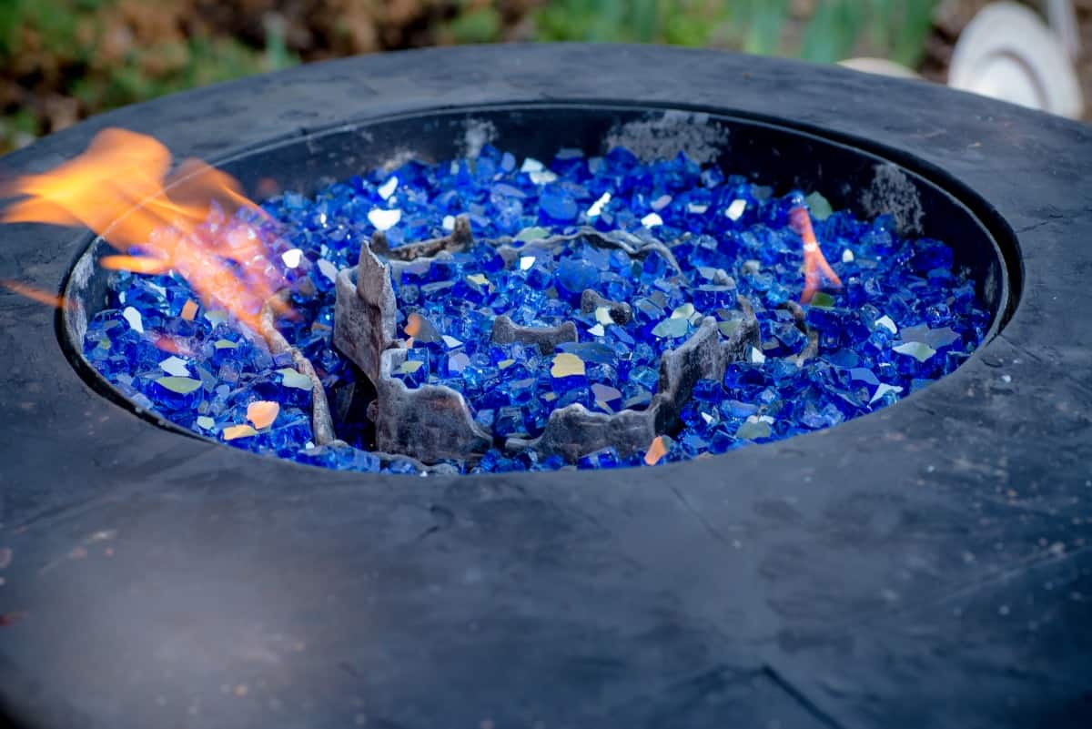 Close up of a lit, propane fueled fire pit filled with blue gl.