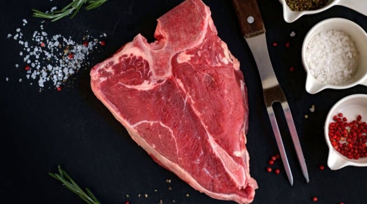 Raw porterhouse steak on a black background with some salt and spices in white dishes.