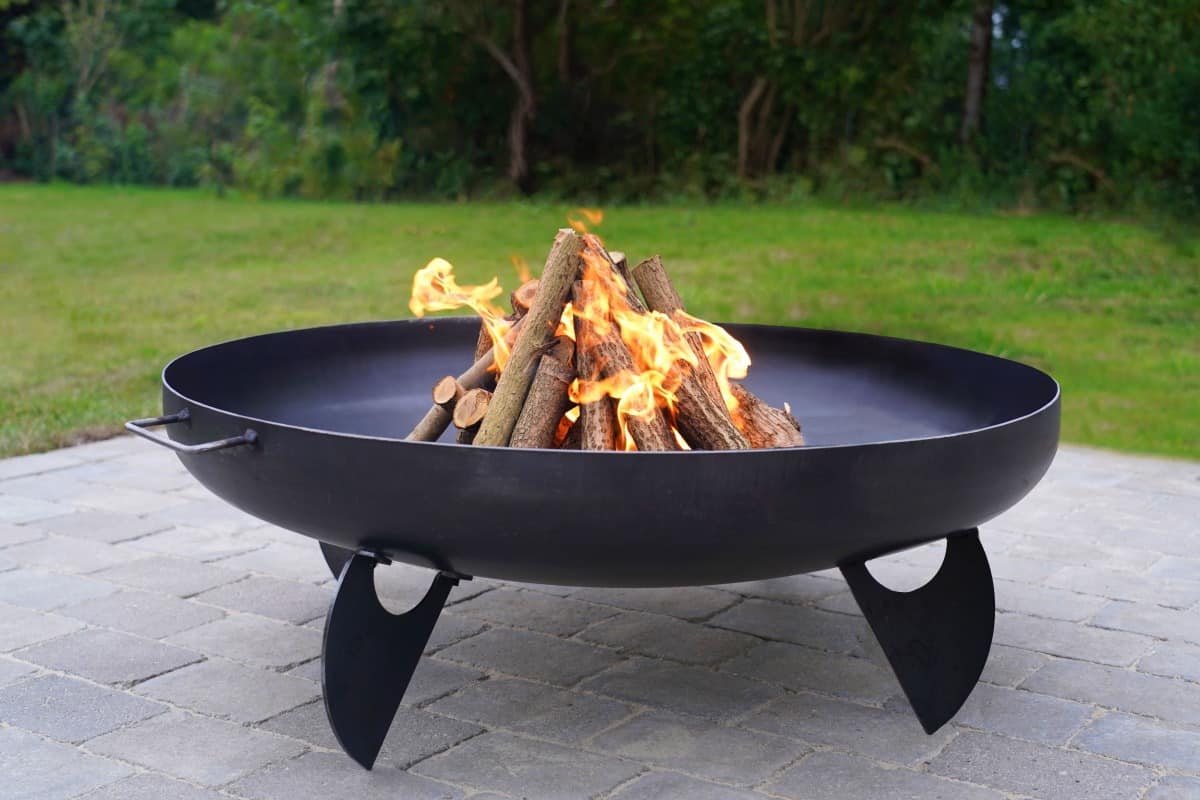 An iron fire pit filled with logs in a pyramid fashion, on f.