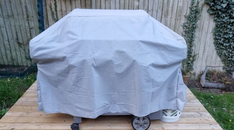 A grill cover, on a gas grill, on a small wooden deck.