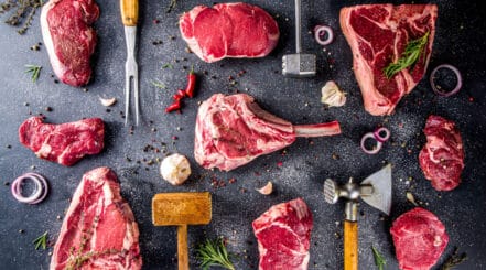 Some of the best steaks for grilling laid out on a dark surface, with spices and kitchen tools