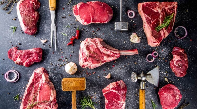Some of the best steaks for grilling laid out on a dark surface, with spices and kitchen tools.