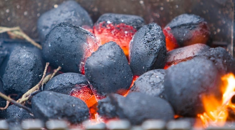 Close up of a small pile of charcoal briquettes being lit from the center.