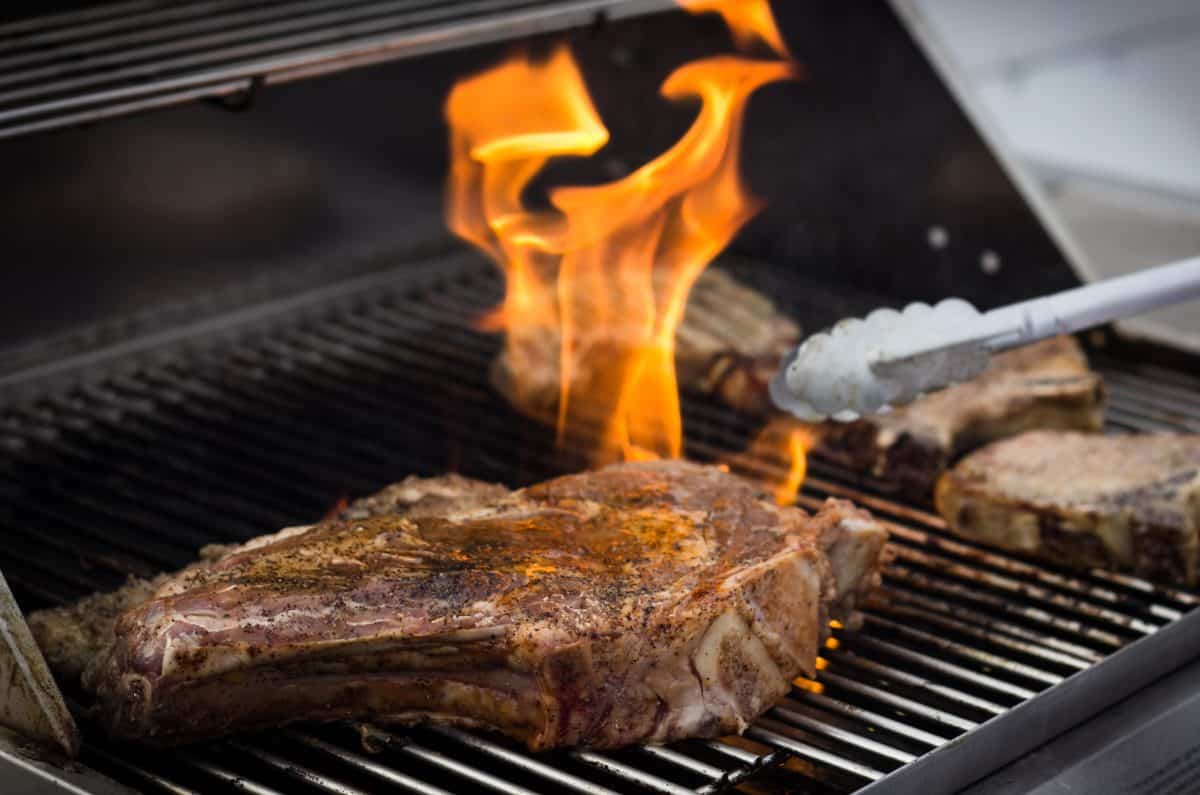 A bone in steak being licked by flames on a gr.