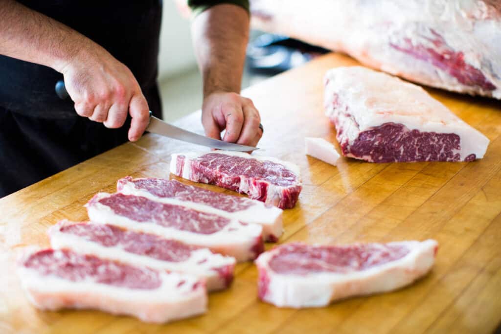 A porter road butcher carving steaks on a ta.