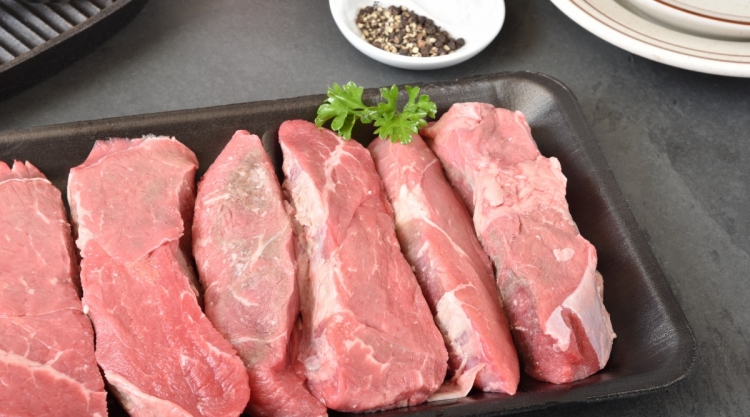 Raw petite sirloin steaks in a tray with one sprig of parsley.